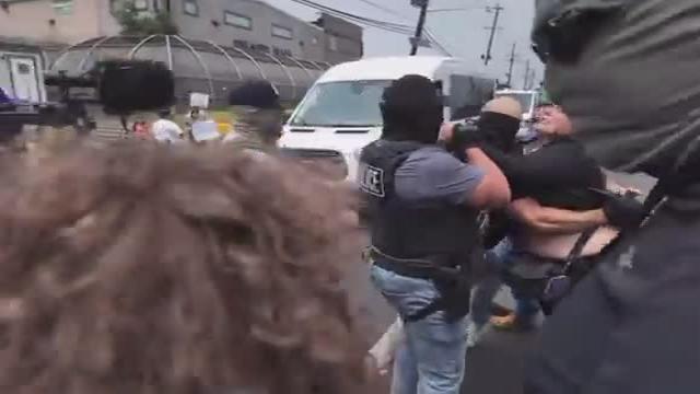 Anti-ICE protesters throw their bodies on the front of an ICE vehicle, and hit the hood with their hands, as the vehicle leaves an ICE detention facility in NJ.  A chunky screaming protester with a shaved head gets pushed to the ground.